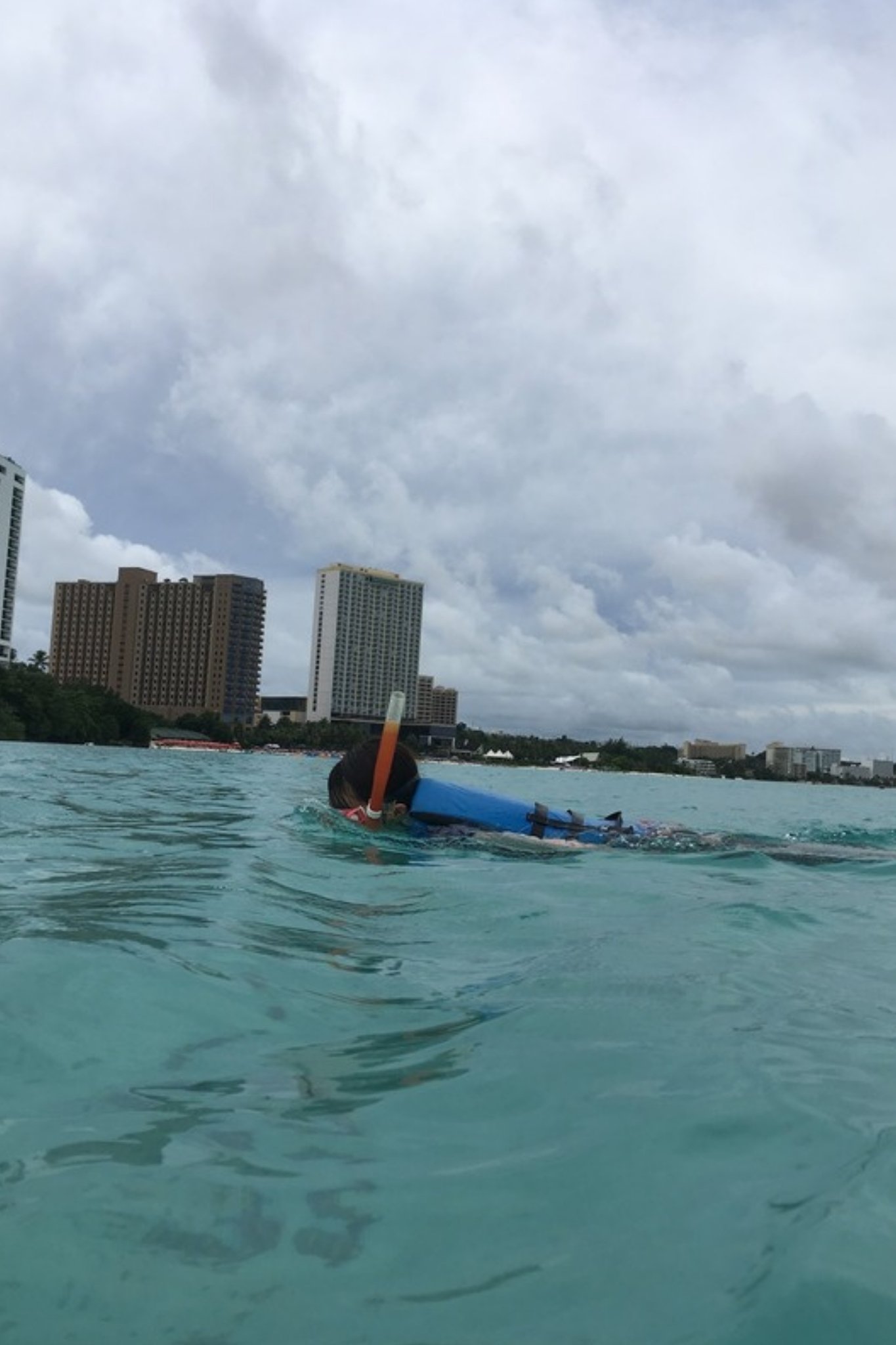 高層ホテル群を背に、タモン湾の海でシュノーケリングをする