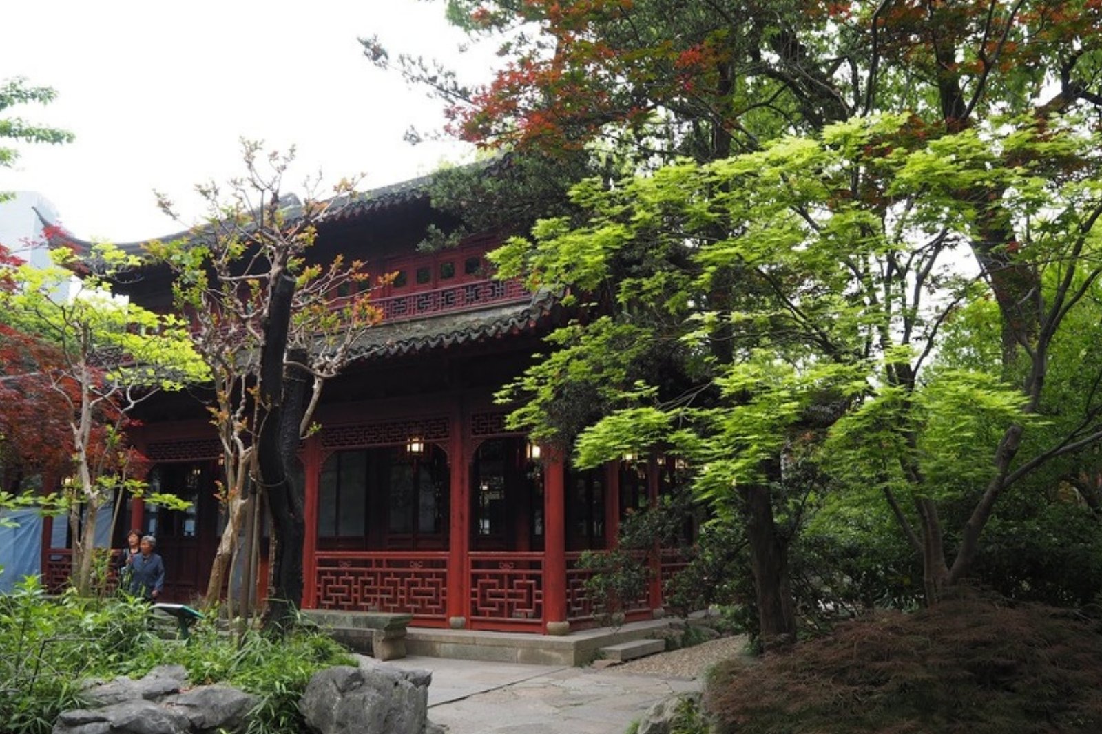 朱色の木造建物と新緑の中国庭園