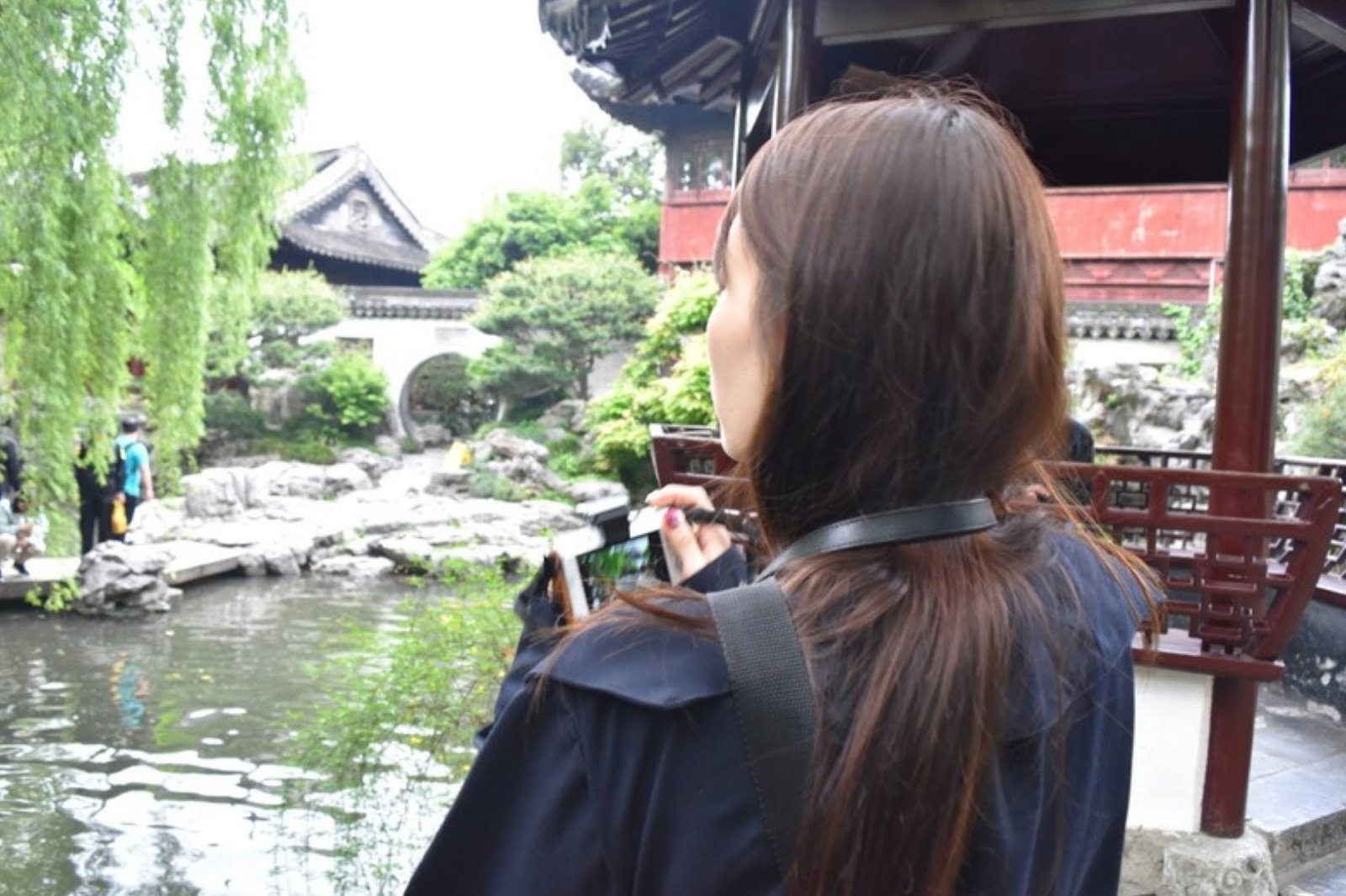 中国庭園の池のほとりで景色を撮影する奥さま